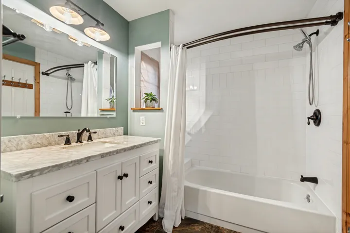 Bathroom featuring a white vanity with a light-toned countertop, a rectangular mirror, and a built-in bathtub with subway tile surround