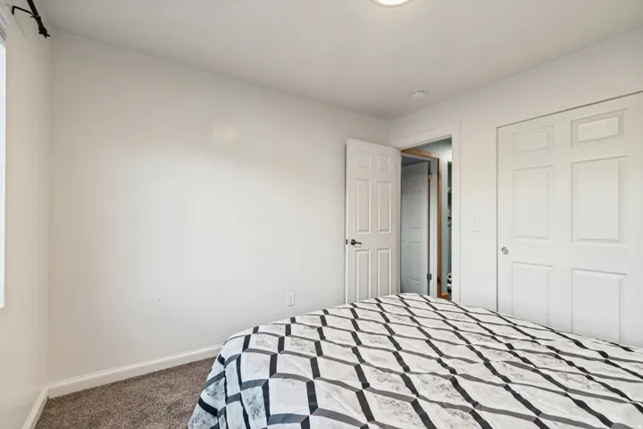 Bedroom featuring neutral wall paint, gray carpet flooring, a single window with a black curtain rod, white baseboards, and two white panel doors