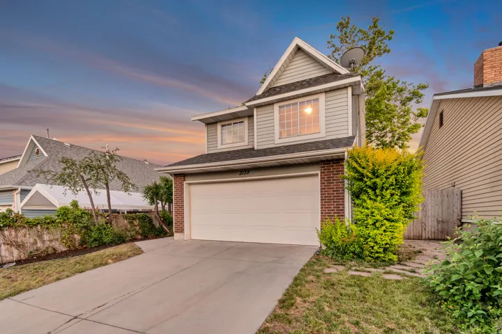 Two-story residence featuring light gray siding with brick accents, an attached garage, and a concrete driveway