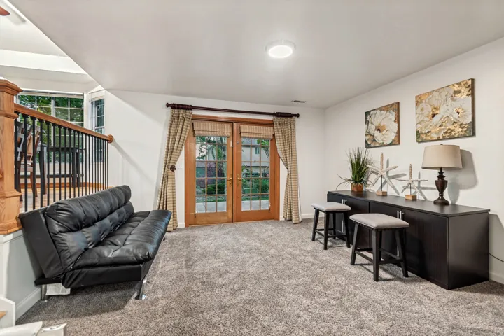 Carpeted lower level featuring a light wood railing, double French doors, and built-in cabinetry