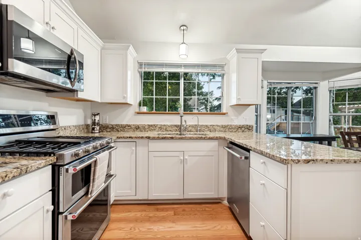 Kitchen featuring white cabinetry, granite countertops, stainless steel appliances, wood-finish flooring, and multiple windows