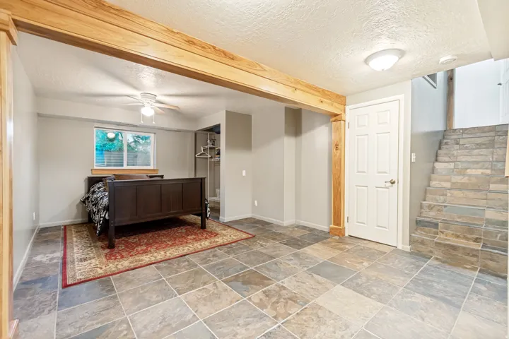 Spacious room featuring large format tile flooring, natural wood beams and columns, and a ceiling fan with integrated lighting