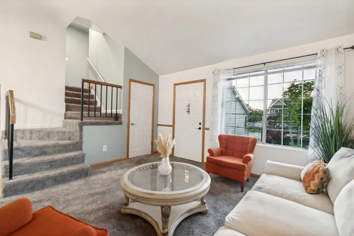 Carpeted living area featuring a prominent staircase with wood and metal railing, a large multi-pane window, and high ceilings