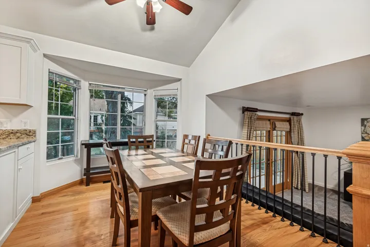 Dining area featuring a bay window, wood-finish flooring, white cabinetry, granite countertops, and a wood ceiling fan