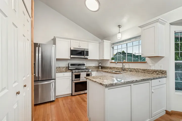 Kitchen featuring vaulted ceilings, wood-finish flooring, white cabinetry, granite countertops, and stainless steel appliances
