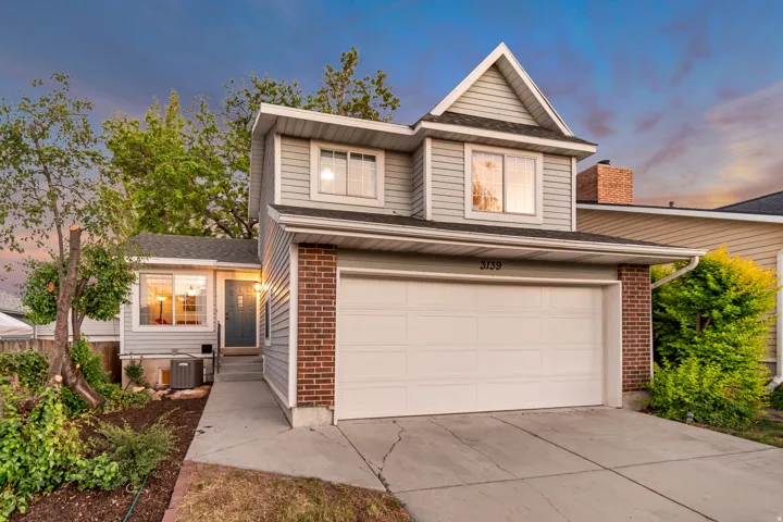 Two-story residence featuring light gray siding, brick accents, and a prominent gable roofline