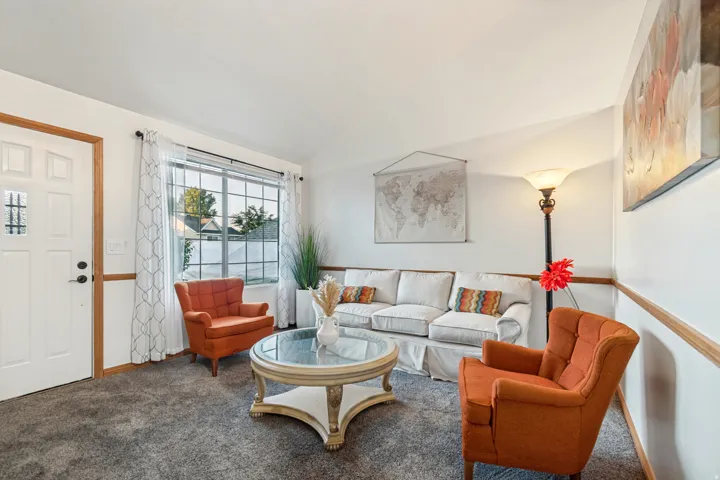 Inviting living area featuring plush gray carpeting, a decorative front entry door with glass inserts, and a large multi-pane window