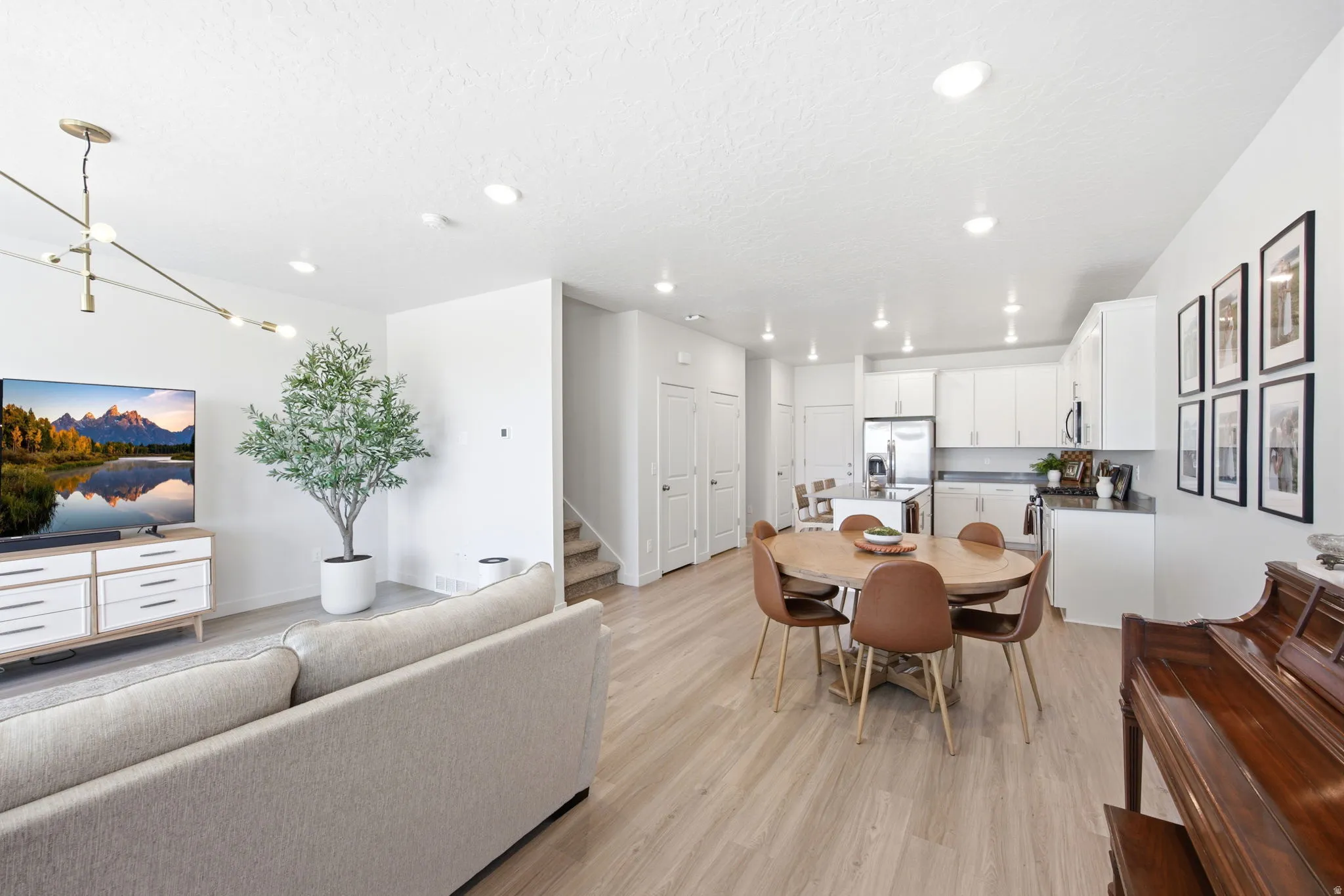Open-concept living space featuring wood-finish flooring, recessed lighting, and a modern linear chandelier
