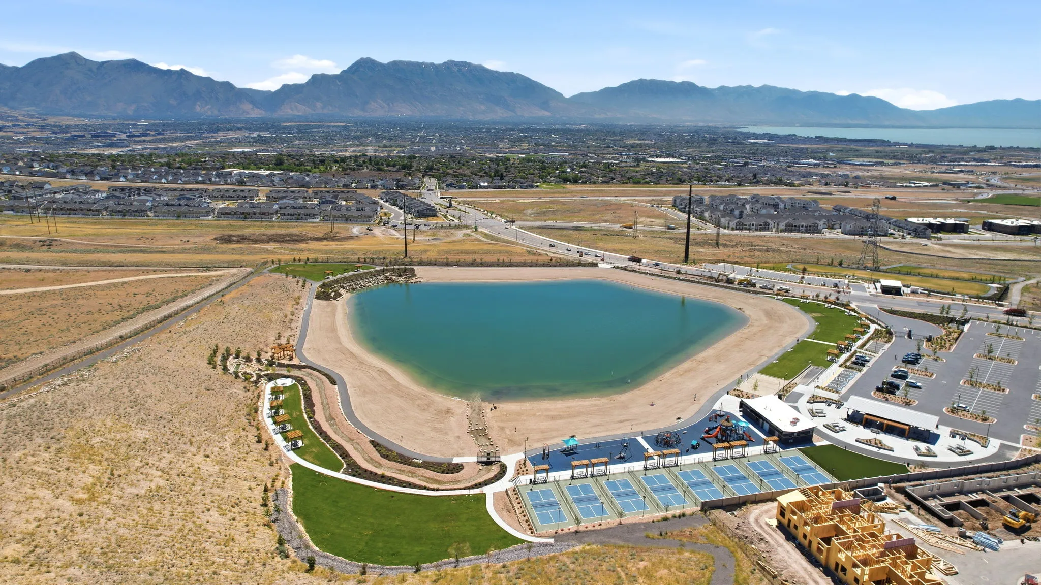 Expansive community recreation area featuring a large central lake with sandy shores, multiple pickleball courts, and a dedicated playground