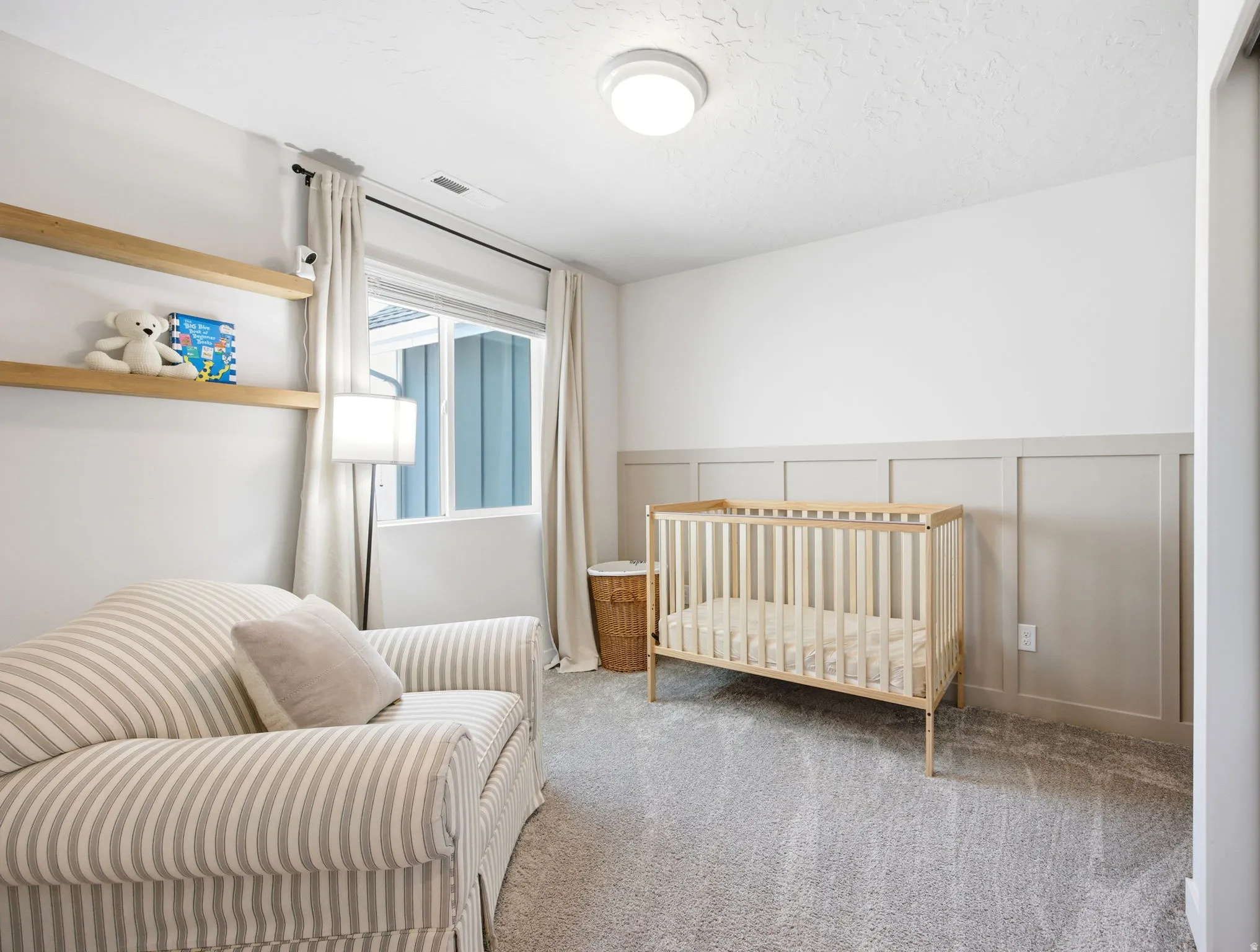 Bright room featuring a single window with curtain rods, wall-mounted shelving, neutral-toned wainscoting, and carpet flooring