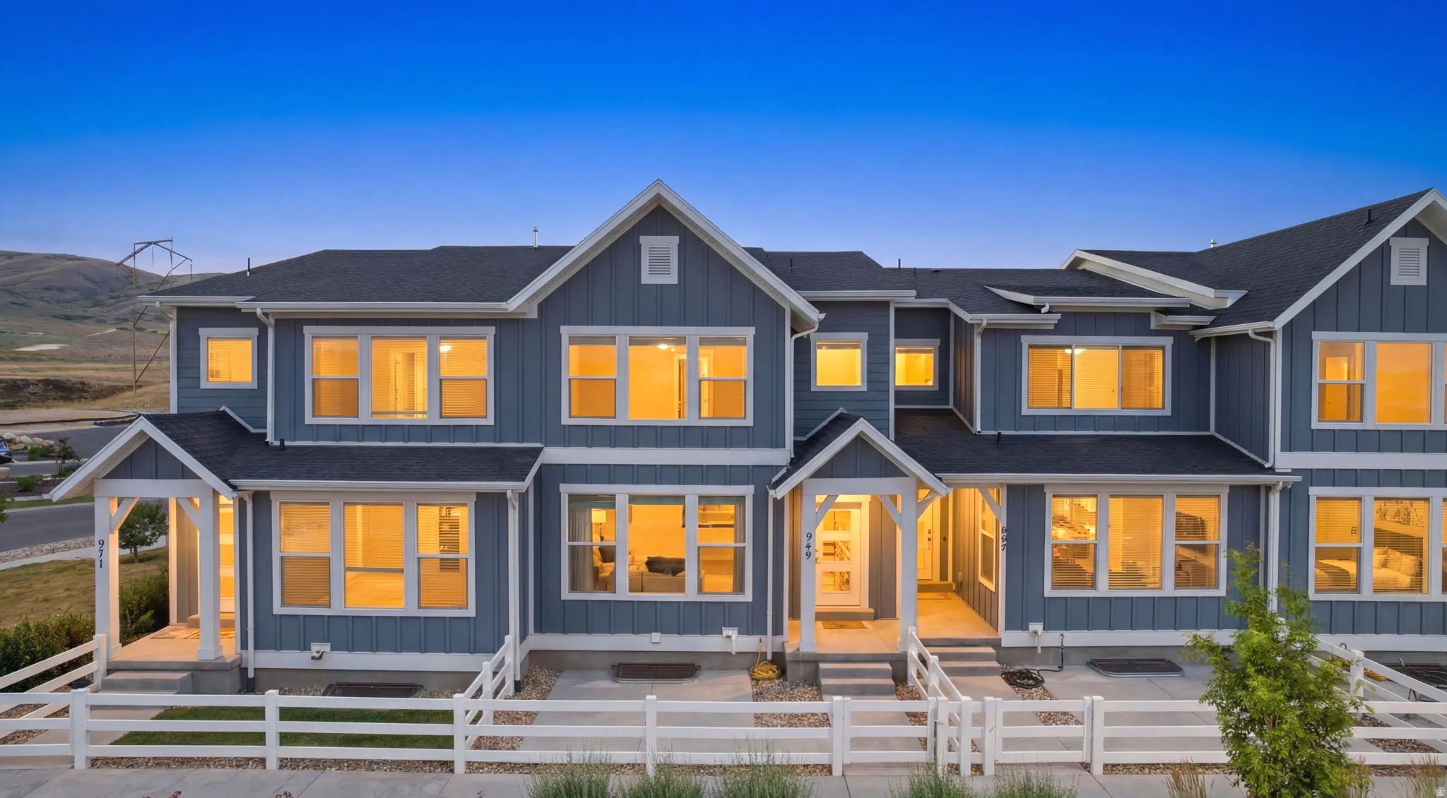 Modern multi-unit residence featuring blue siding with white trim, multiple gables, a dark shingle roof, and white picket fencing