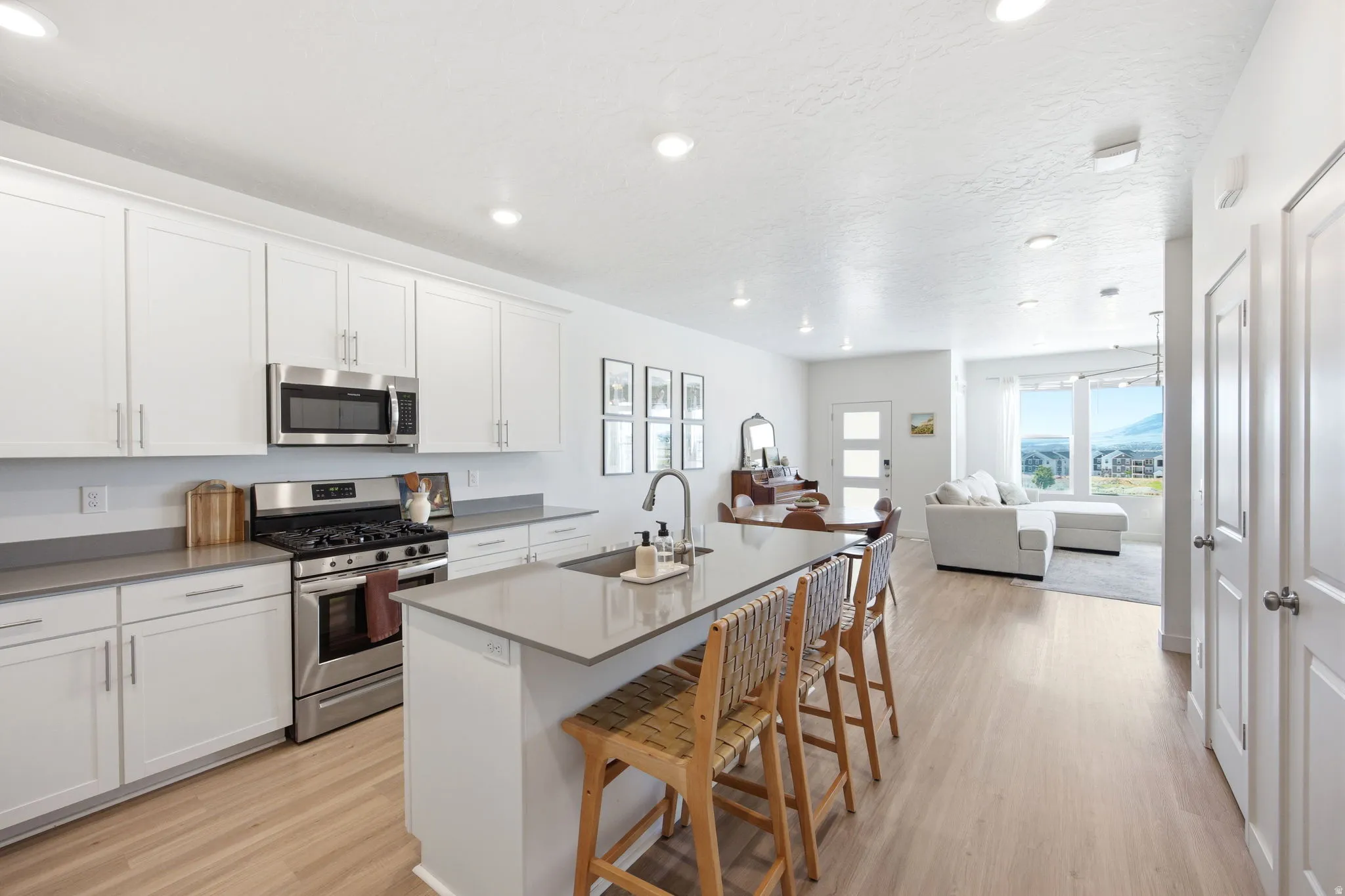 Modern kitchen featuring white shaker cabinetry, stainless steel appliances, a center island with an undermount sink, grey countertops, and wood-finish flooring