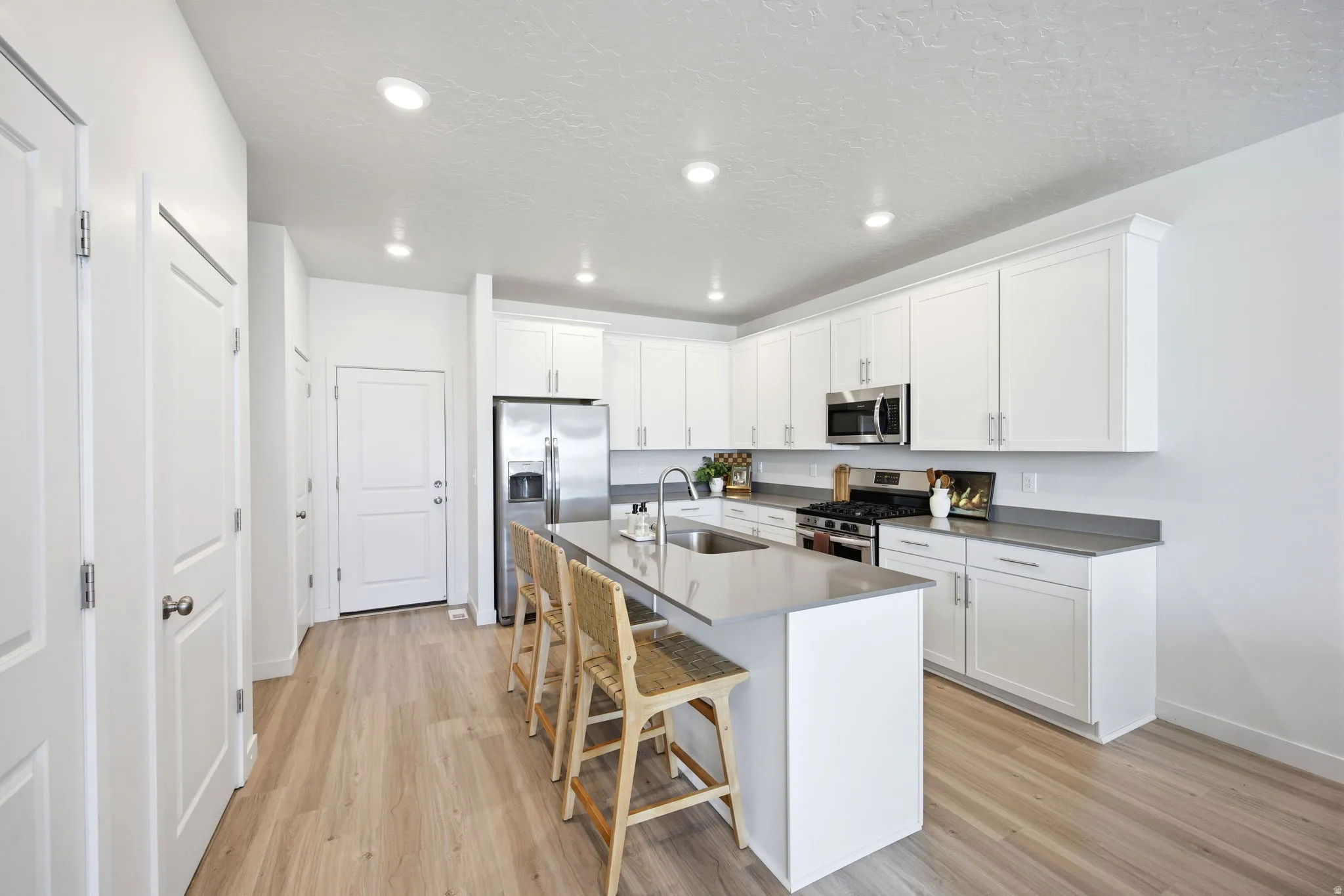 Bright kitchen featuring white shaker cabinetry, stainless steel appliances, a center island with counter seating, light wood-finish flooring, and recessed lighting