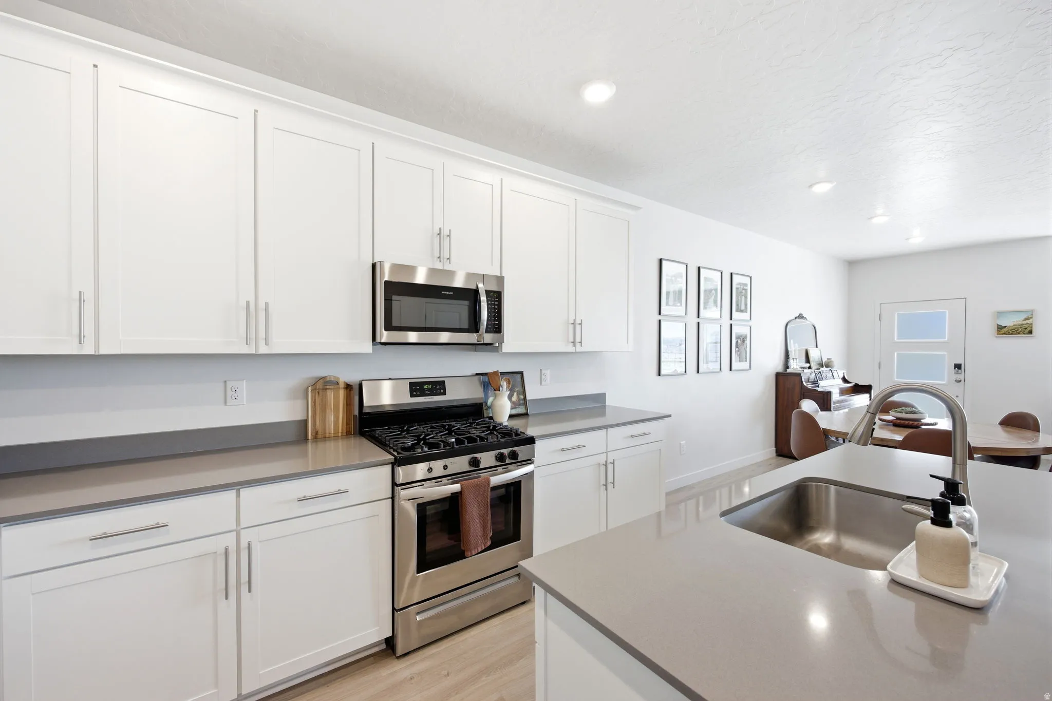 Modern kitchen featuring white shaker cabinetry, stainless steel appliances, light gray countertops, a large island with an undermount sink, and wood-finish flooring