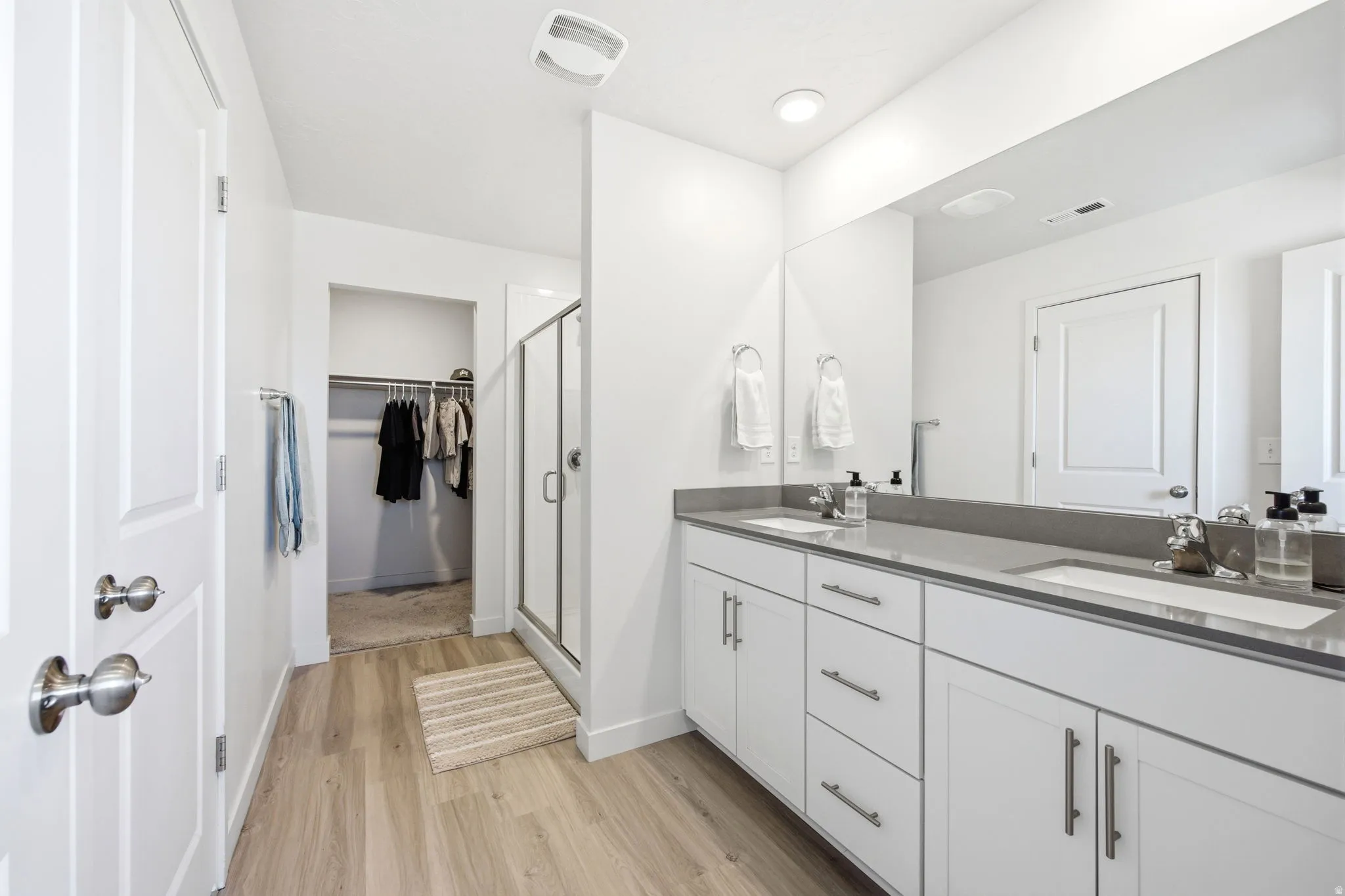 Bathroom featuring wood-finish flooring, a double vanity with grey countertops, dual rectangular undermount sinks, and an expansive mirror
