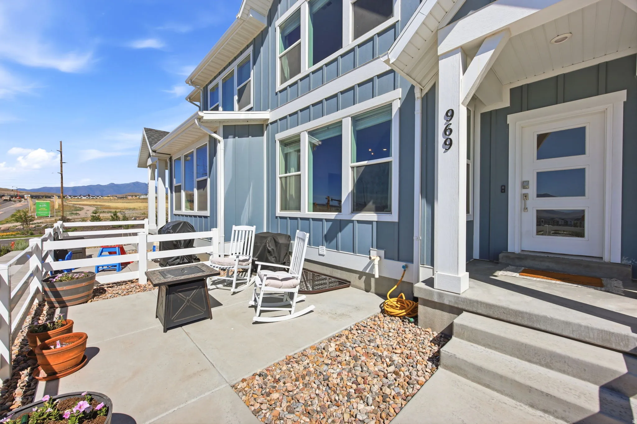 Contemporary exterior featuring board and batten siding, multiple large windows, a modern entrance door with three frosted glass panels, and a concrete patio with a white perimeter railing