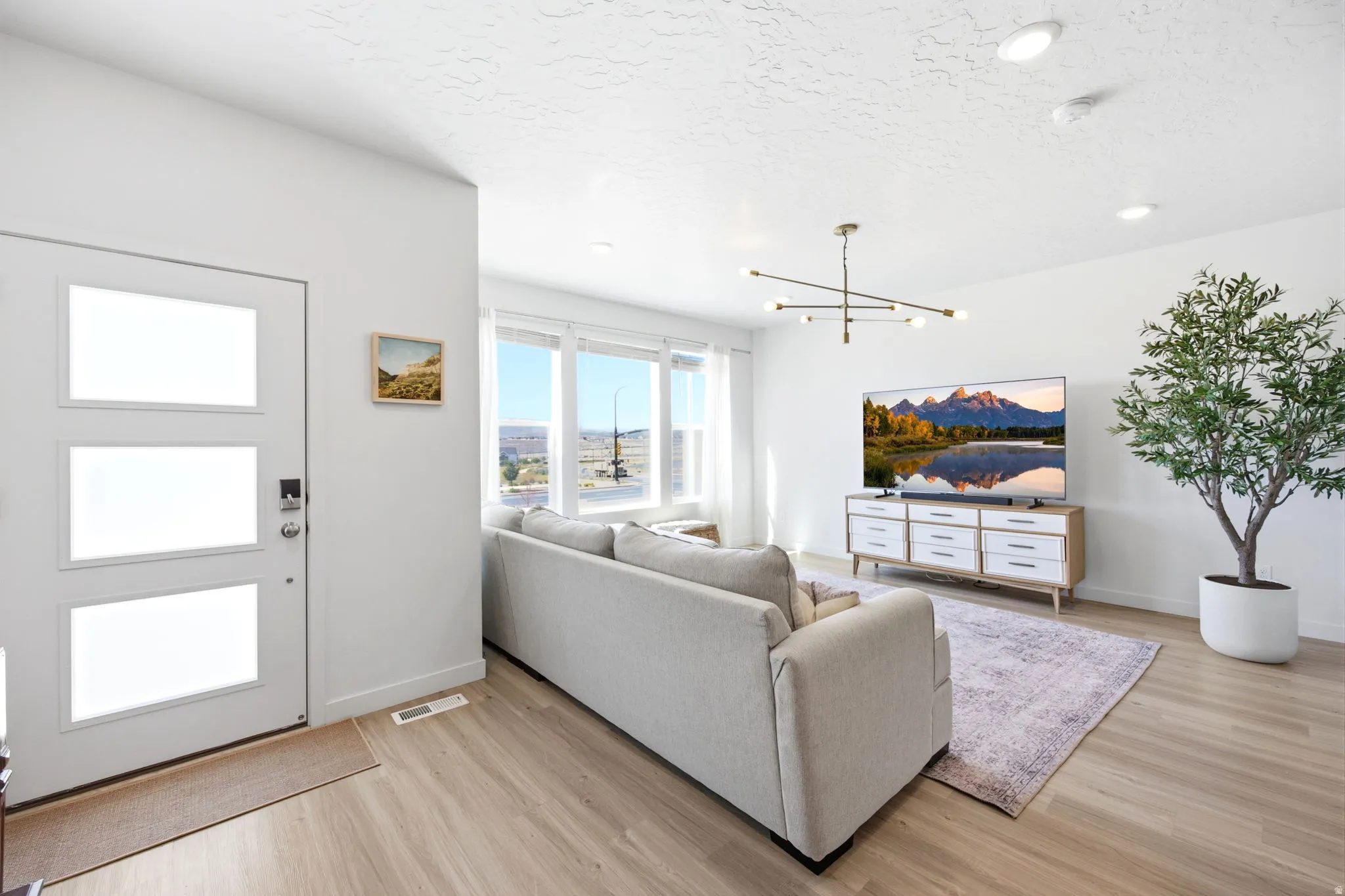 Bright living area featuring wood-finish flooring, a contemporary light fixture, and a wall of windows offering distant scenery