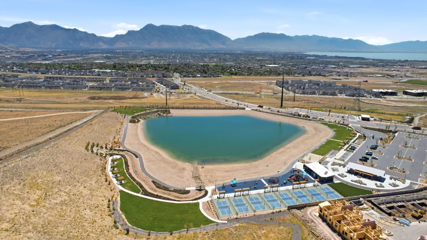 Expansive community recreation area featuring a large central lake with sandy shores, multiple pickleball courts, and a dedicated playground