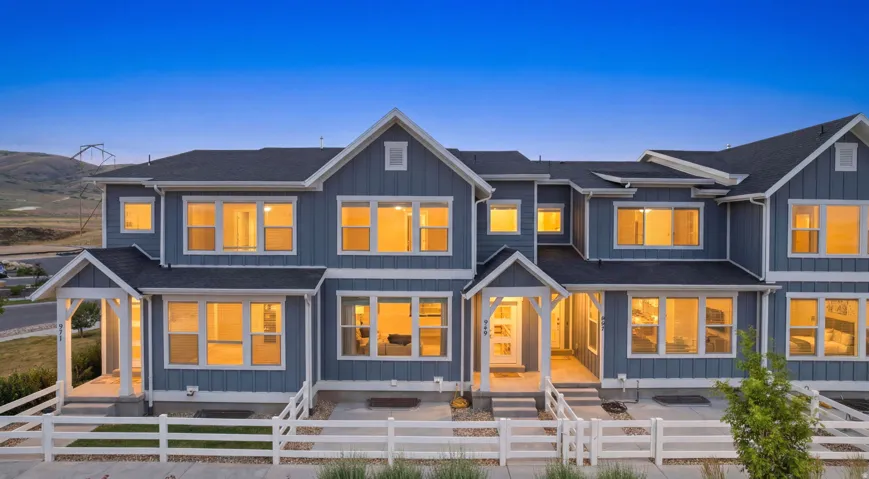 Modern multi-unit residence featuring blue siding with white trim, multiple gables, a dark shingle roof, and white picket fencing