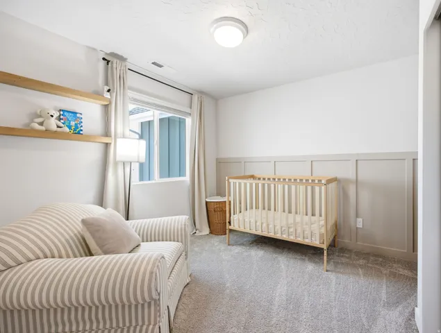 Bright room featuring a single window with curtain rods, wall-mounted shelving, neutral-toned wainscoting, and carpet flooring