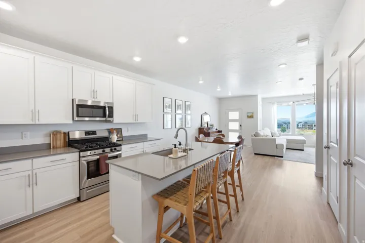 Modern kitchen featuring white shaker cabinetry, stainless steel appliances, a center island with an undermount sink, grey countertops, and wood-finish flooring