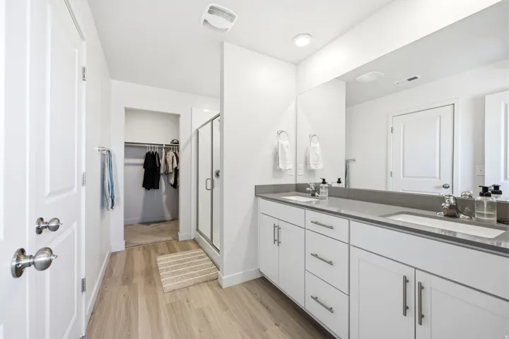 Bathroom featuring wood-finish flooring, a double vanity with grey countertops, dual rectangular undermount sinks, and an expansive mirror
