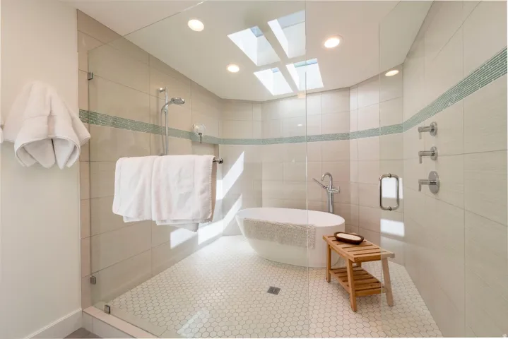 Glass-enclosed shower with a freestanding soaking tub, mosaic accent tile, skylights, recessed lighting, and hexagon floor tile
