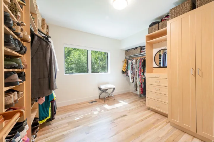 Spacious walk-in closet featuring extensive built-in shelving, wood-finish flooring, and a large window providing natural illumination