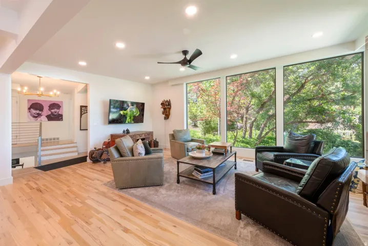 Spacious living area featuring expansive floor-to-ceiling windows, wood-finish flooring, recessed lighting, a contemporary ceiling fan, and a built-in staircase with a metal and glass railing
