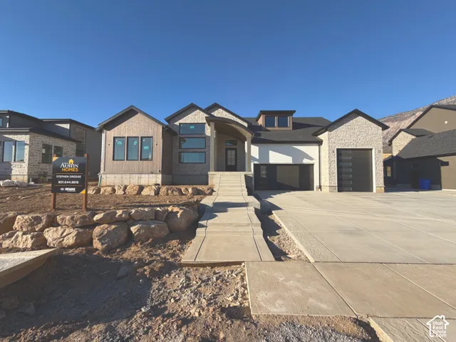 Modern exterior with mixed material siding, elevated concrete walkway, concrete driveway, and black garage doors