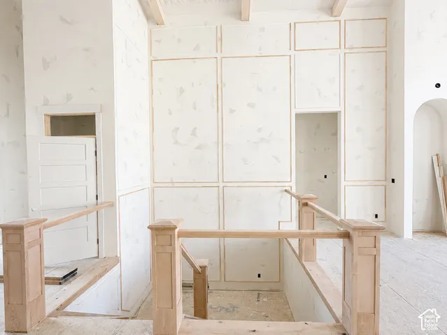 Exposed ceiling beams, recessed lighting, architectural wall paneling, arched doorway, and wood-finish stair railing