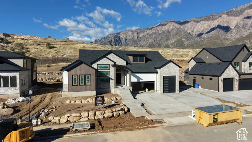 Multi-gabled exterior featuring brick and panel siding, dark-toned asphalt shingle roof, integrated multi-car garage, concrete driveway, and prominent mountain backdrop