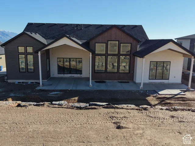 Rear exterior featuring a multi-gabled roofline, dark composite siding, floor-to-ceiling windows, and a covered concrete patio
