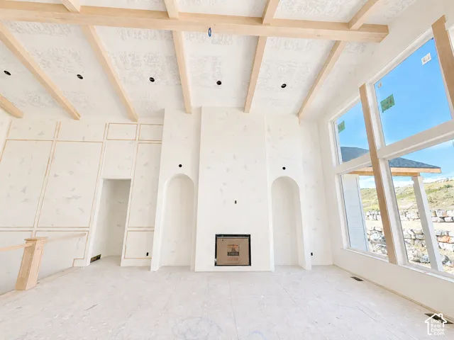 Vaulted ceiling with exposed wood beams, large-format windows, integrated fireplace, wall paneling, and arched wall niches