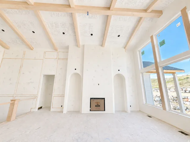 Vaulted ceiling with exposed wood beams, large-format windows, integrated fireplace, wall paneling, and arched wall niches