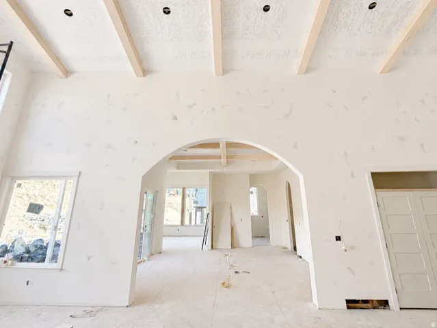 Exposed wood ceiling beams, arched doorways, a large window, and a paneled door
