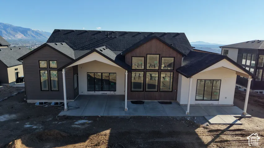 Rear exterior featuring mixed-material siding, multiple covered concrete patios, extensive multi-pane window arrays, and a mountain backdrop
