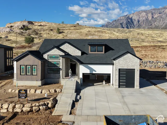 Contemporary exterior featuring a stone and siding facade, multi-gabled roofline, concrete driveway, and mountain backdrop