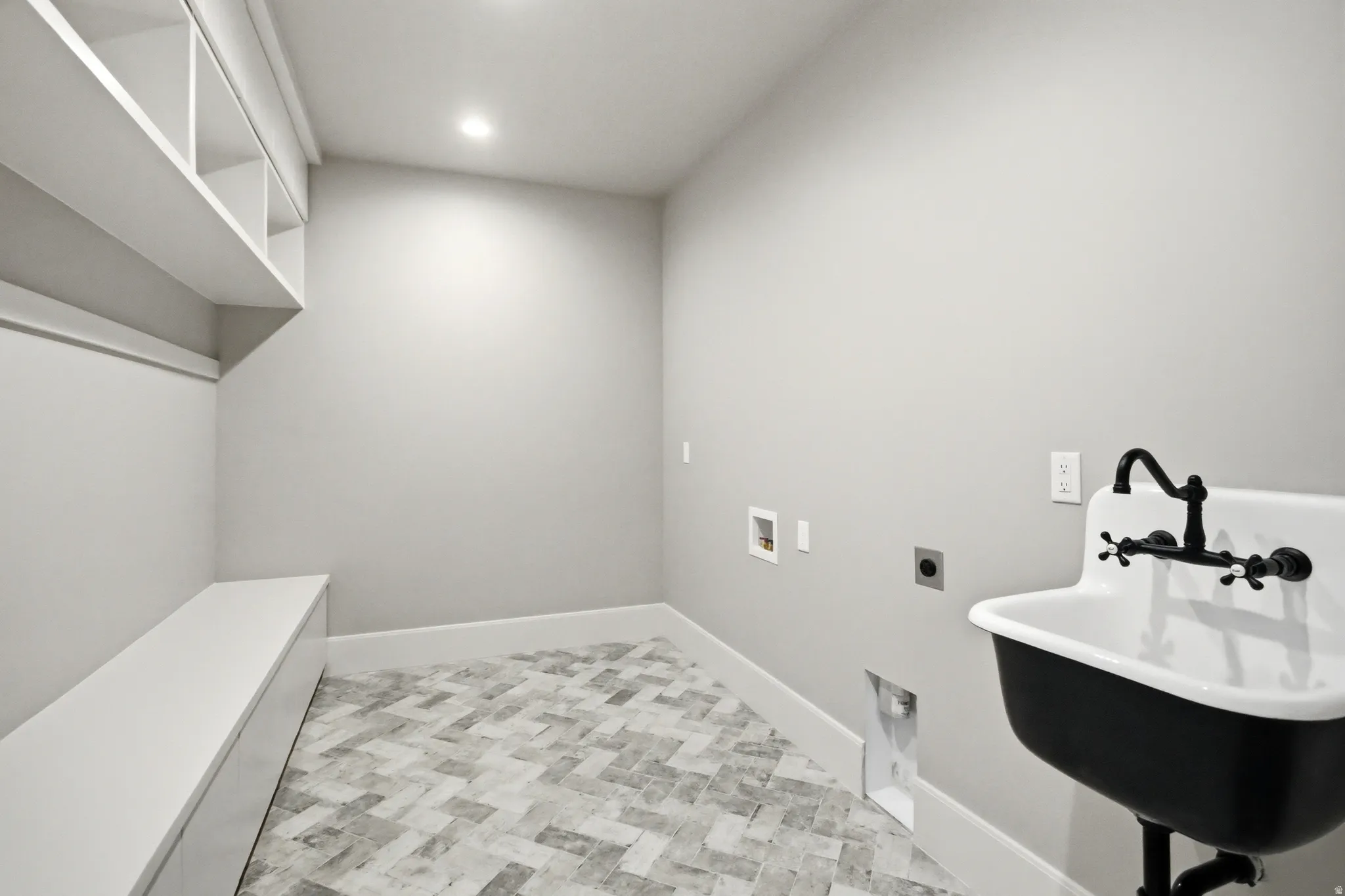 Utility room featuring herringbone pattern tile flooring, recessed lighting, built-in shelving, a storage bench, and a wall-mounted utility sink with a black faucet