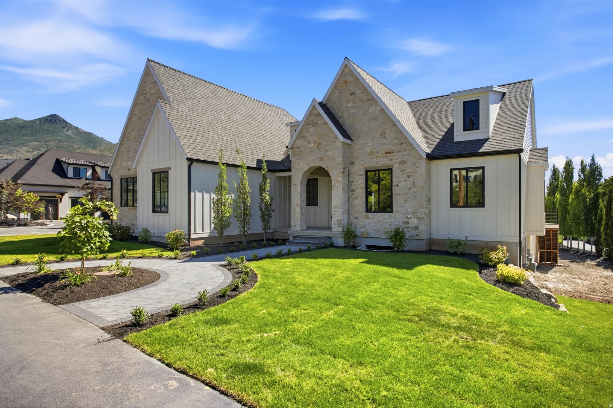 Contemporary dwelling featuring a stone and vertical siding facade, gabled rooflines, black-framed windows, and an arched entry