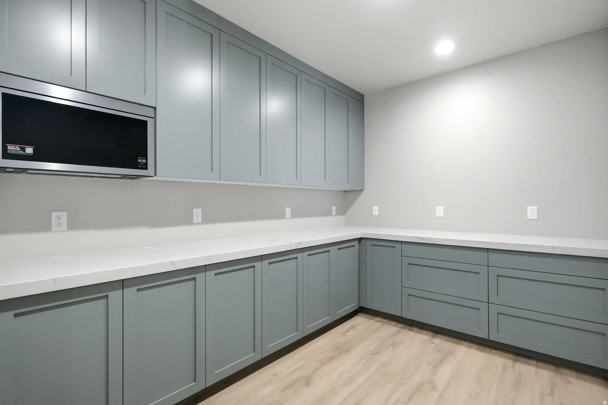 Spacious pantry featuring extensive light gray cabinetry, light wood-finish flooring, white countertops, and a built-in microwave