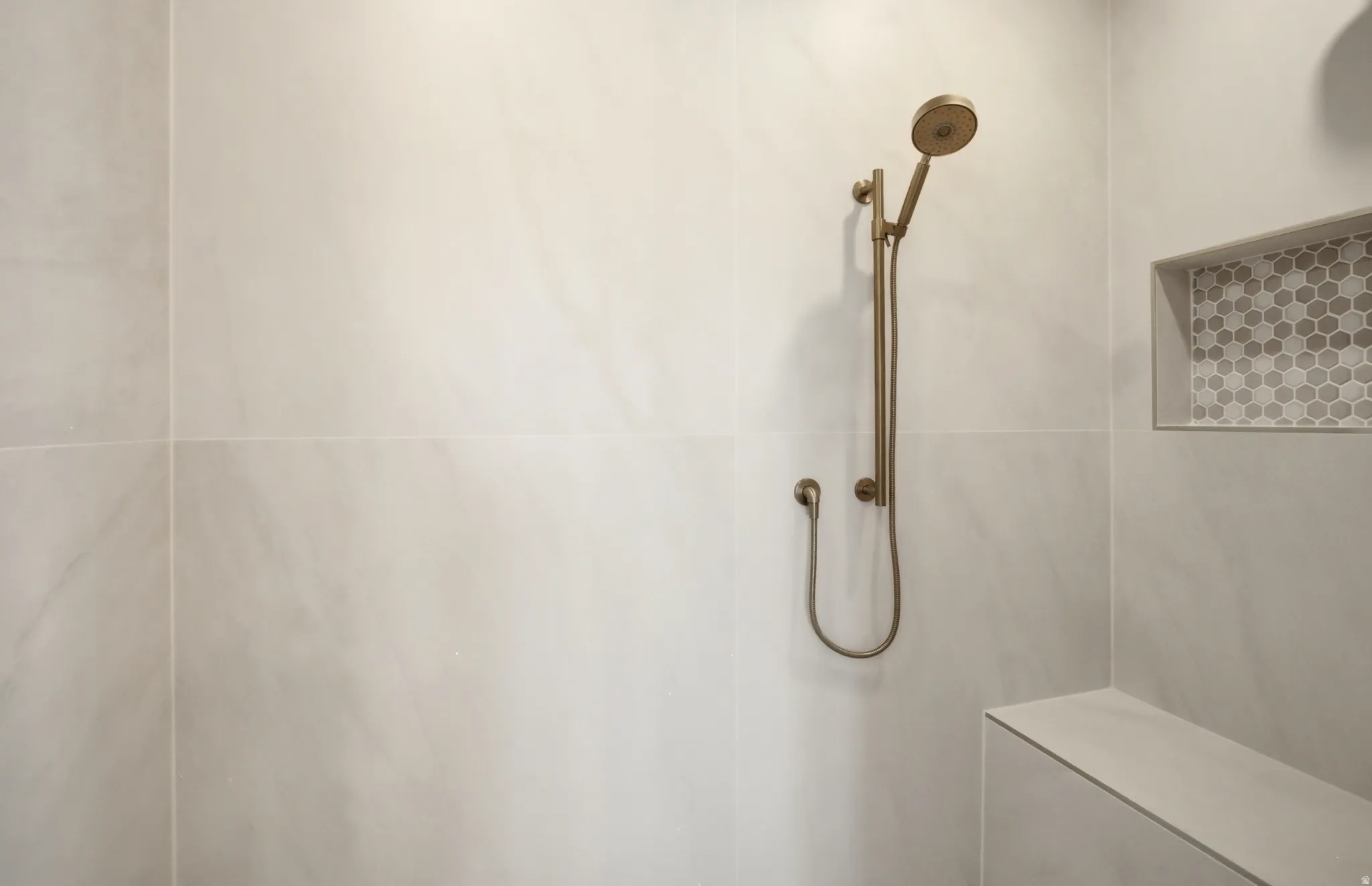 Shower featuring large format wall tiling, a built-in bench, and a recessed niche with mosaic hexagon tile