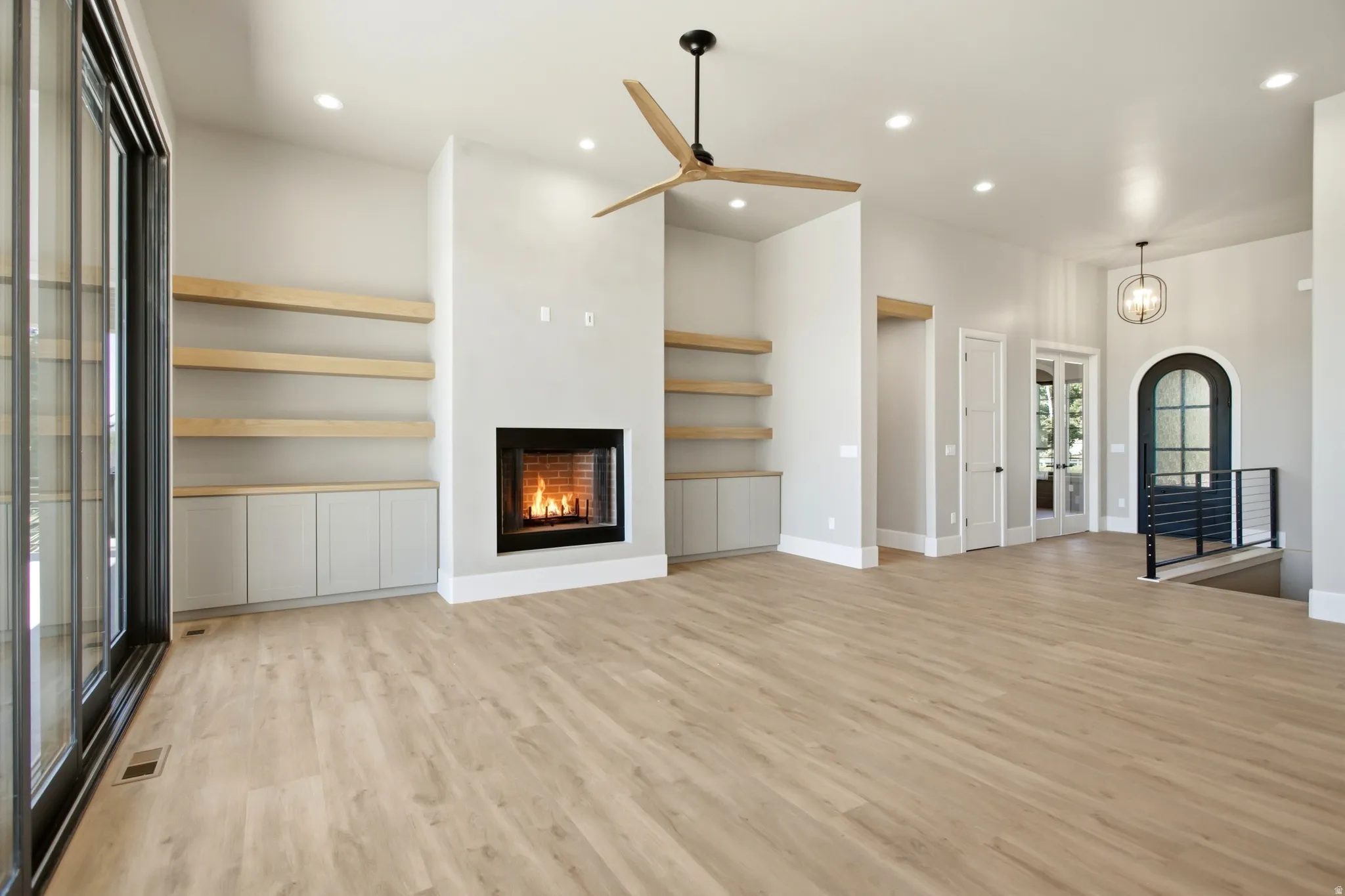 Spacious open-concept room featuring a contemporary fireplace, custom built-in shelving with lower cabinetry, recessed lighting, and a large sliding glass door
