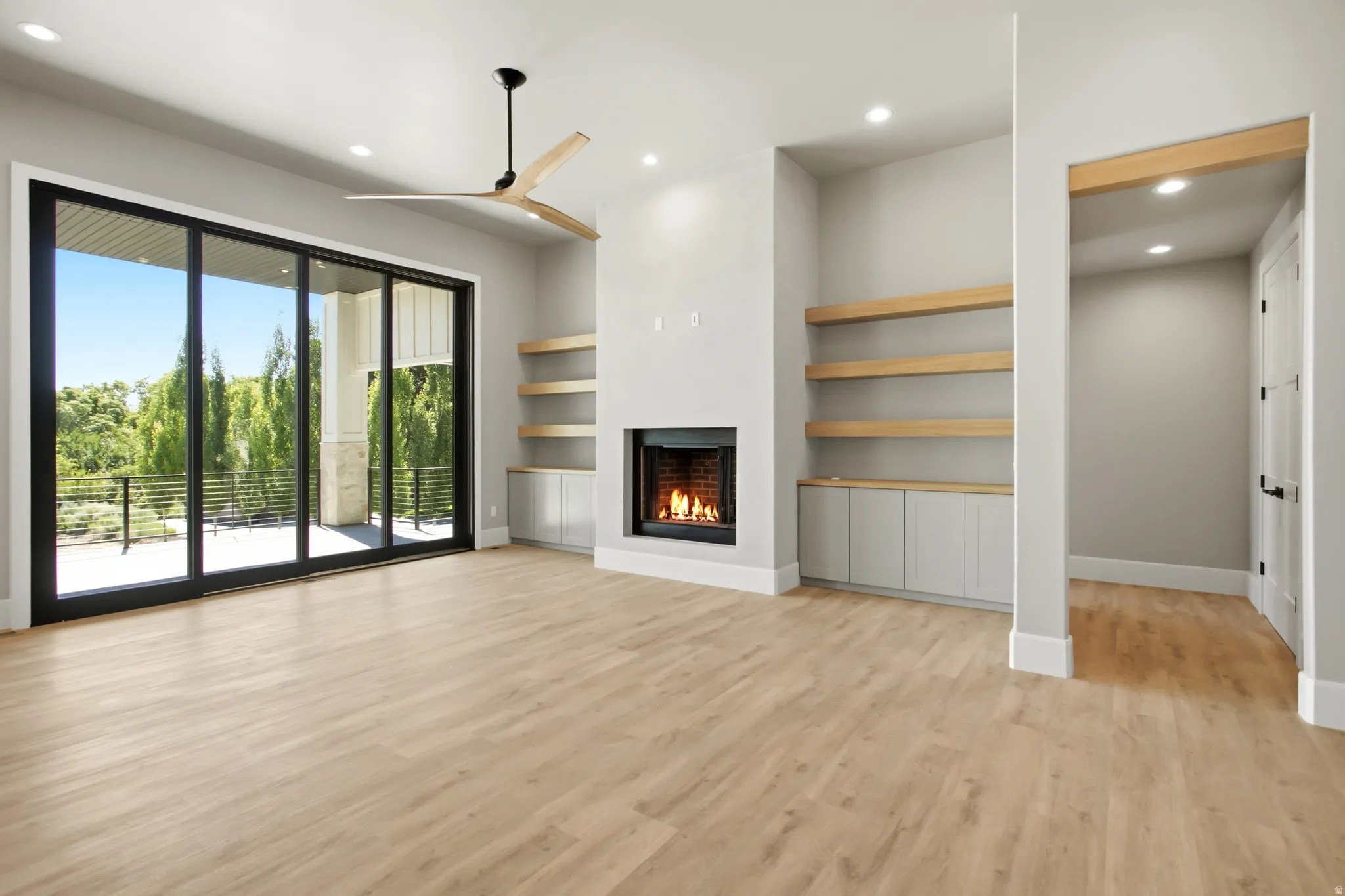 Spacious living area featuring expansive sliding glass doors, a contemporary fireplace, built-in shelving with base cabinetry, and a modern ceiling fan