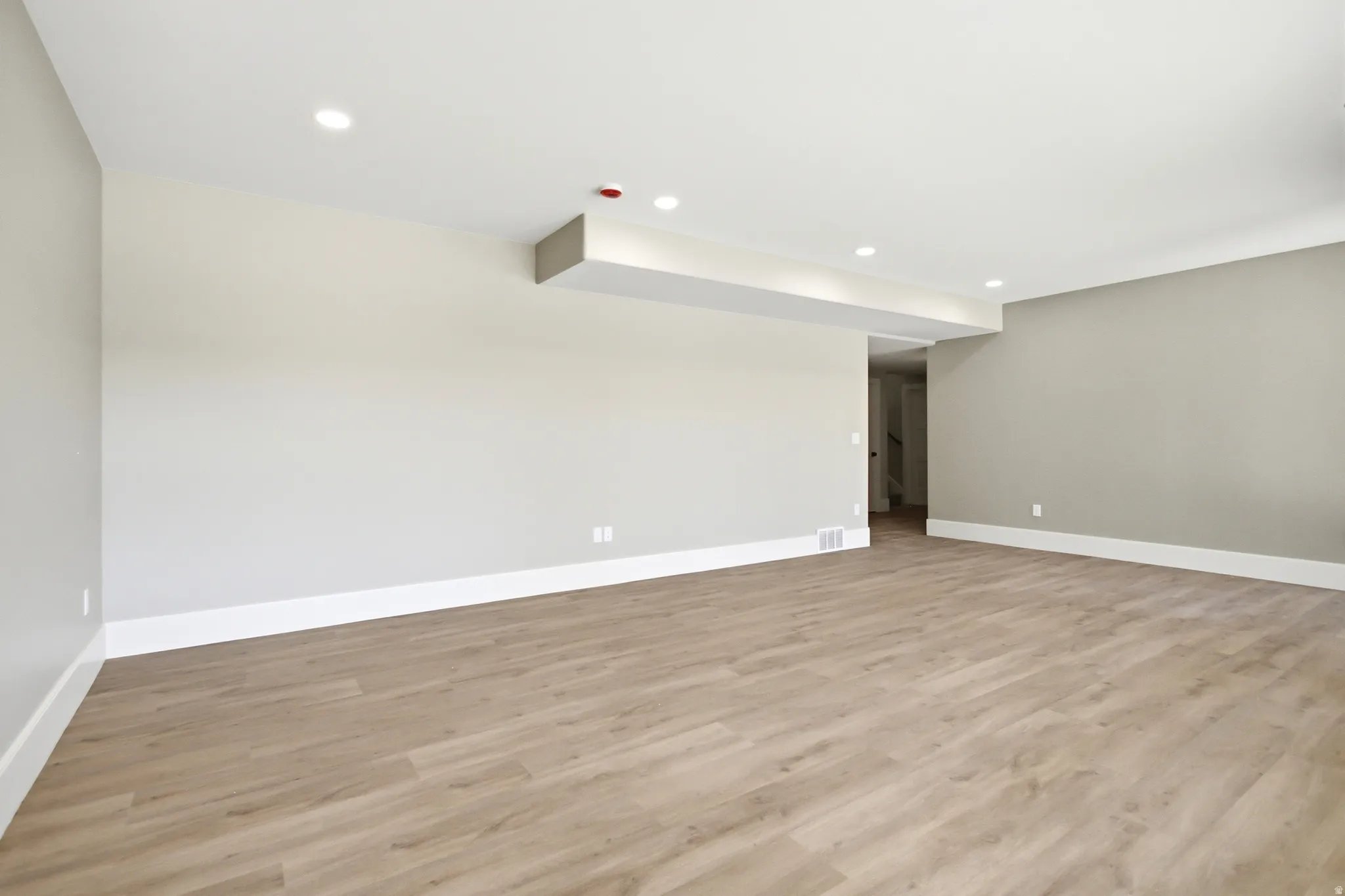 Spacious interior room featuring light-toned walls, recessed lighting, and white baseboards