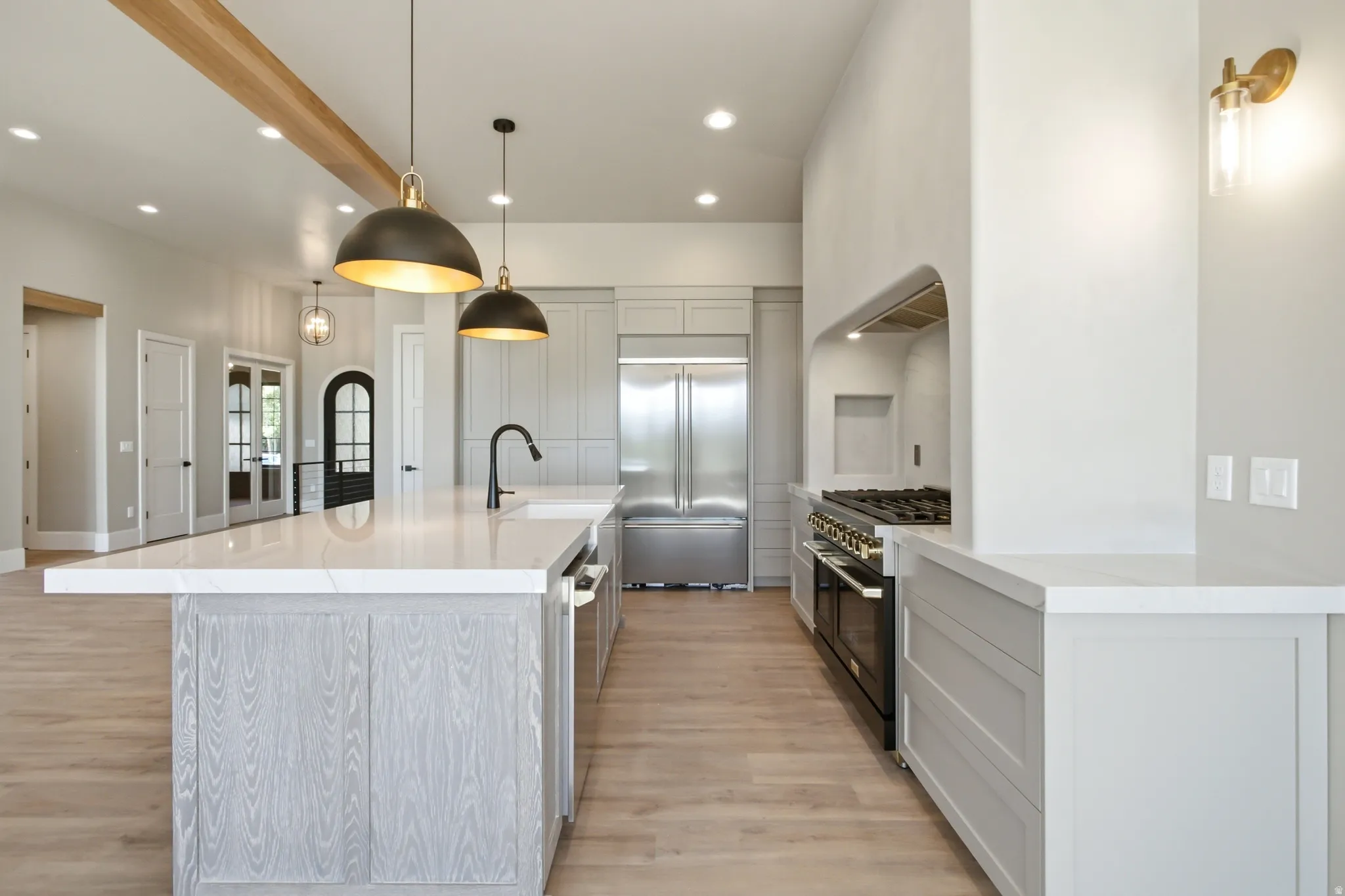 Open-concept kitchen featuring an oversized island with a white countertop and wood-finish cabinetry, a large stainless steel refrigerator, a professional-grade range, a built-in wall oven, and a recessed range hood within an arched alcove