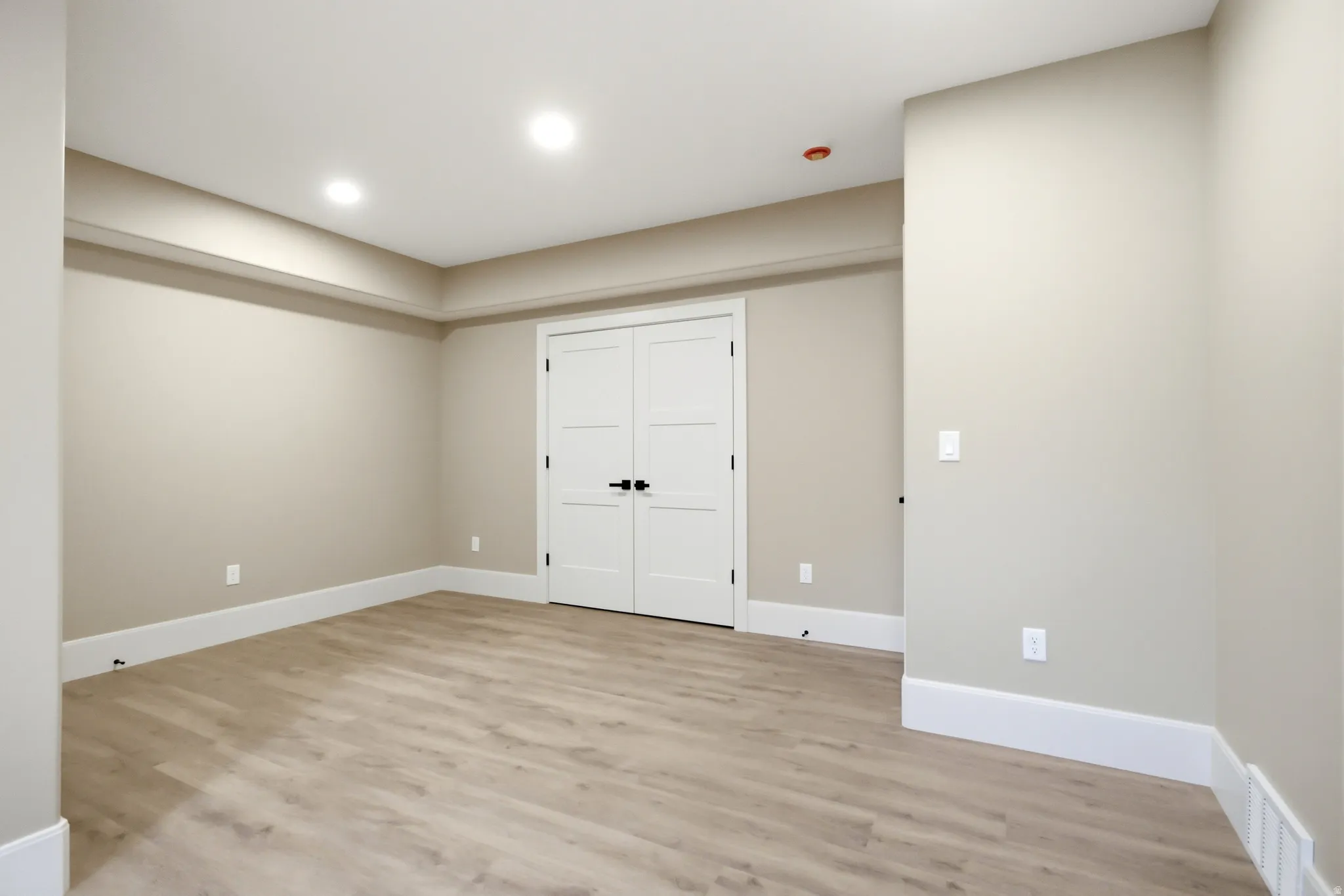 Spacious room featuring light wood-finish flooring, recessed lighting, and a neutral wall palette