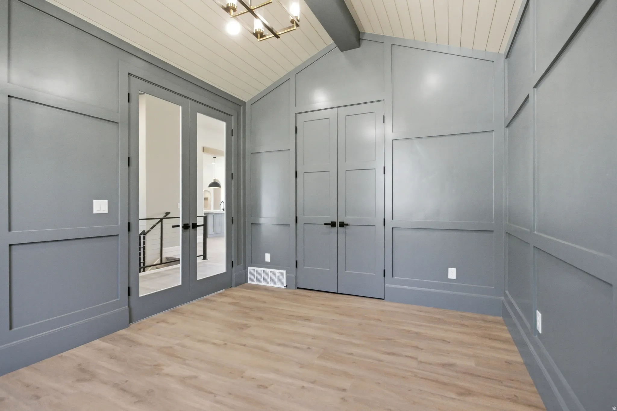 Spacious room featuring board and batten wall paneling, vaulted ceiling with wood-finish planks, and light wood-finish flooring