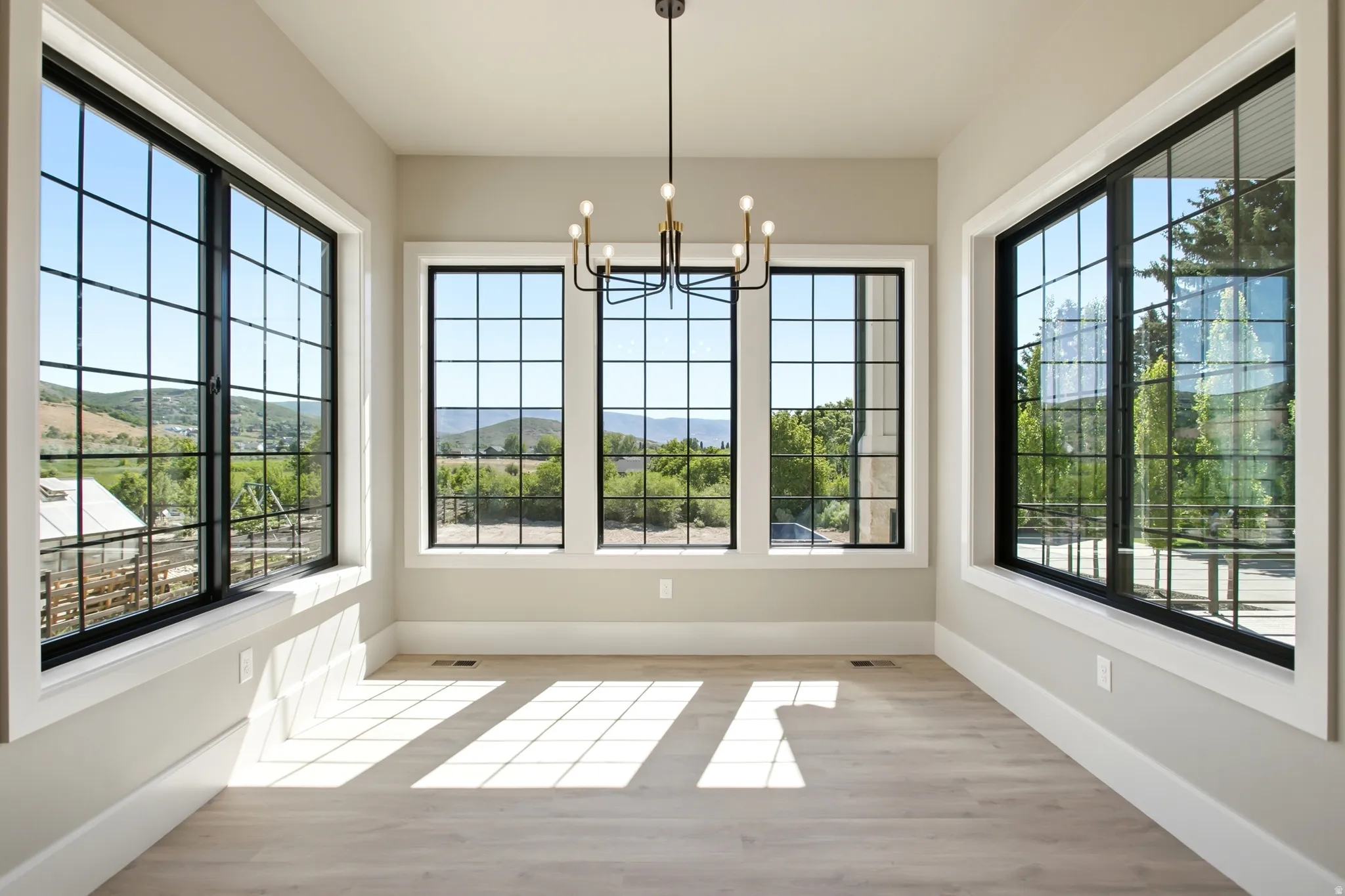 Spacious dining room featuring a contemporary black and gold chandelier, and multiple large black-framed windows with grid patterns