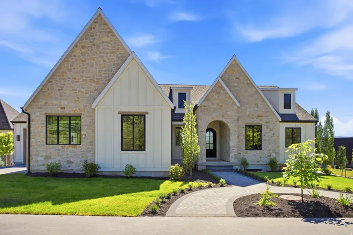 Contemporary residence featuring stone and board-and-batten siding, black-framed windows, an arched entryway, and a paver walkway